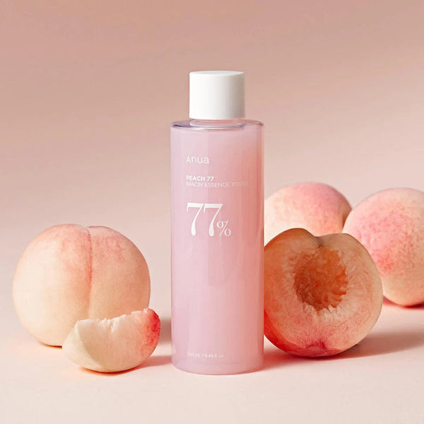 A pink bottle of Anua Peach 77% Niacin Essence Toner with peach fruit extracts, alongside fresh peaches on a pink background.