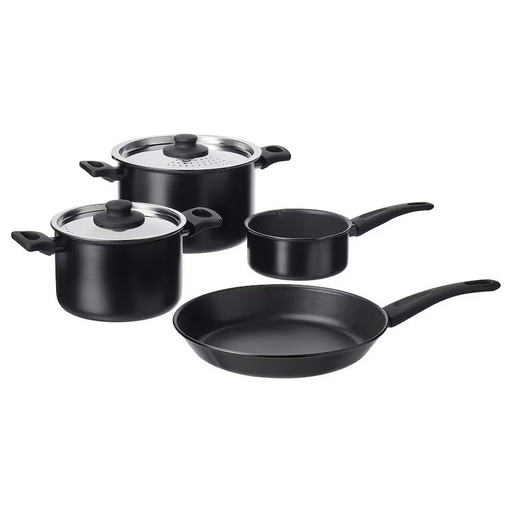 A set of black aluminum cookware including two pots with lids and four frying pans, all with handles.